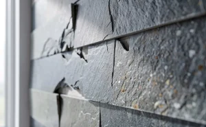 Feuilles minces de pierre collées sur un mur moderne gris, avec les bords légèrement décollés et montrant des imperfections.