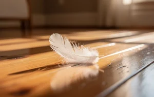 Une plume blanche repose sur un parquet éclairé par la lumière du matin dans une maison paisible.