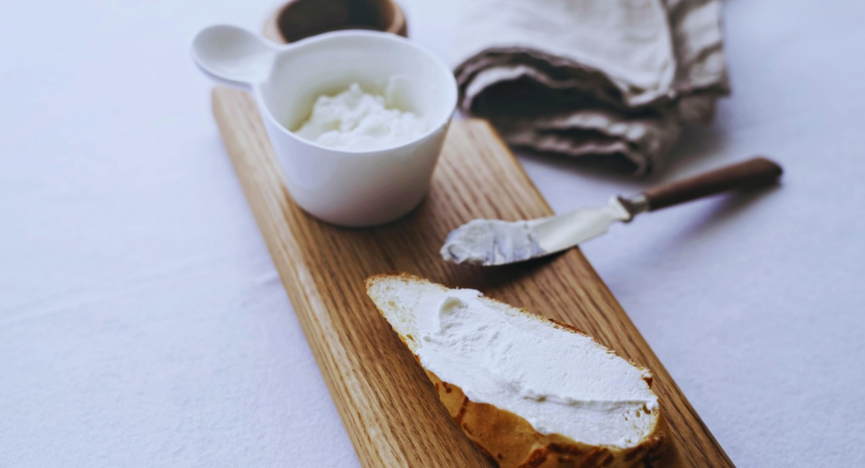 Fromage frais tartiné sur une tranche de pain avec un bol en arrière-plan