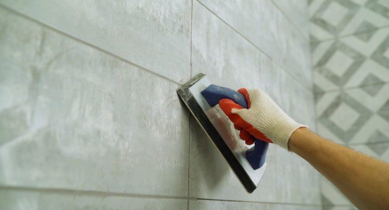 Artisan appliquant du joint gris entre des carreaux muraux